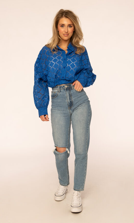 Trendy dames mom jeans met een gat. Een blauwe korte broderie blouse